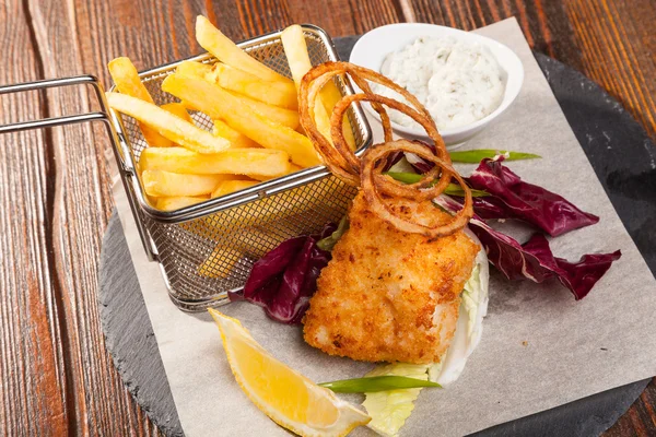 fish with fries and tartar sauce on wooden table