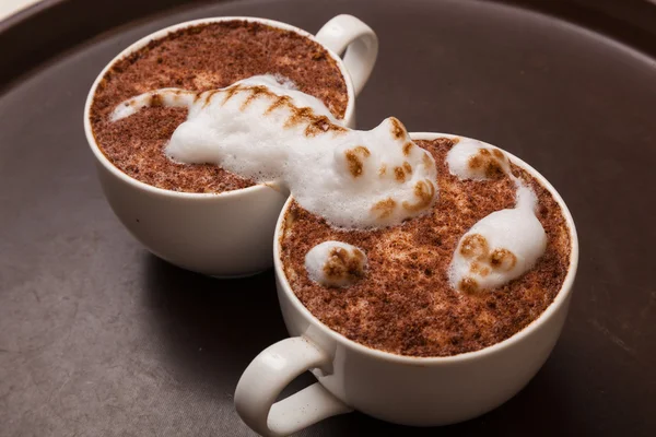 Coffee with foam in the form of a cat and a mouse on brown table