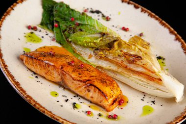 Siyah arka planda ızgara lahana ve somon bifteği.