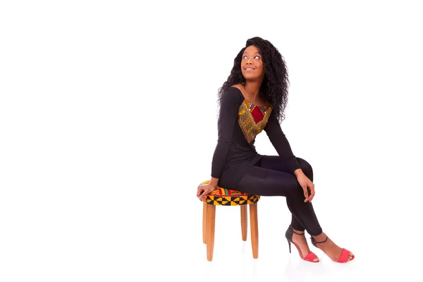 Beautiful African American woman sitting on a stool isolated on — Stock Photo, Image