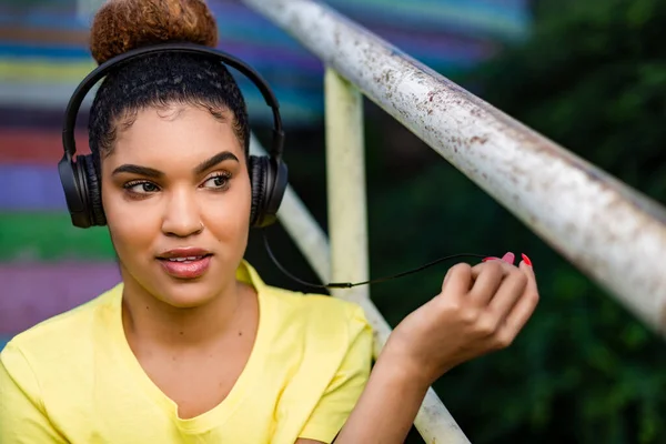 若い黒人アフリカ系アメリカ人の女性がヘッドフォンの屋外で音楽を聴く — ストック写真