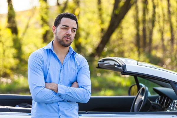 Junger lateinamerikanischer Fahrer sitzt auf der Seite seines neuen Autos — Stockfoto