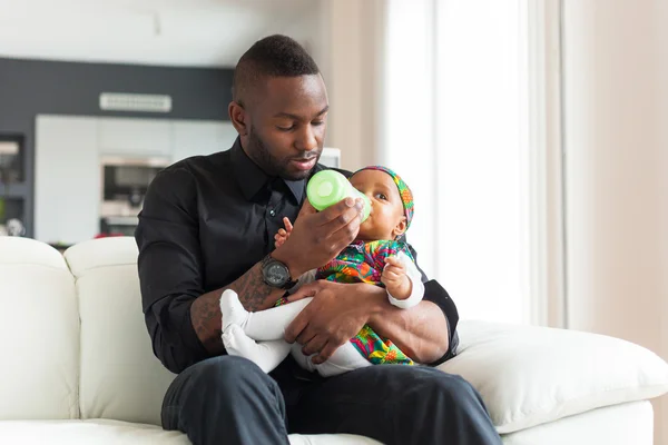 Joven afroamericano padre dando leche a su bebé niña en un — Foto de Stock