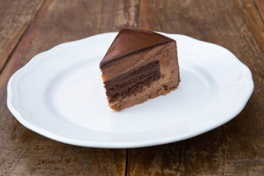 Beyaz tabakta üç farklı çikolatayla nefis bir parça pasta. Ahşap arkaplan.