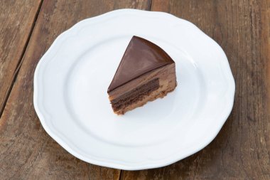 Beyaz tabakta üç farklı çikolatayla nefis bir parça pasta. Ahşap arkaplan.