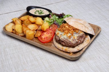 Dilimlenmiş biftekli hamburger ve arkaplanda patates dilimleri.