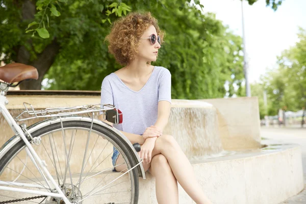 Donna seduta nel parco accanto alla bicicletta — Foto Stock