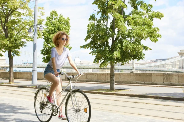 Giovane donna in bicicletta attraverso la città — Foto Stock