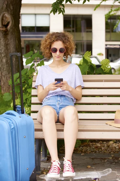 Женщина с чемоданом сидит на скамейке — стоковое фото
