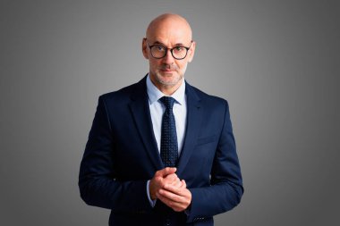 Gri arka planda dikilirken kendine güvenen iş adamının stüdyo portresi. 