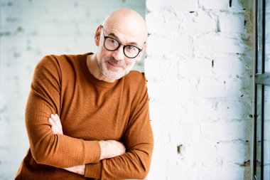  Duvarda durup kameraya bakarken sakallı ve gözlüklü meraklı bir adamın portresi..