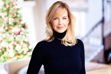 Portrait shot of smiling blond woman standing in her standing room with christmas tree in the background.  clipart