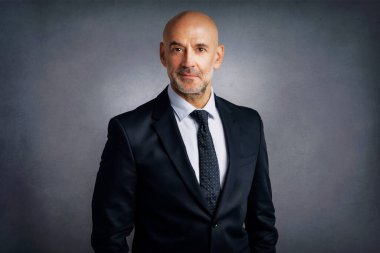 Gri arka planda dikilirken kendine güvenen iş adamının stüdyo portresi. 