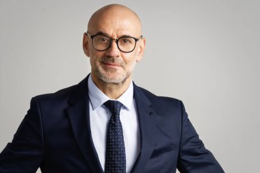 İzole edilmiş açık gri arka planda dururken takım elbise giyen kendine güvenen işadamının stüdyo portresi. 