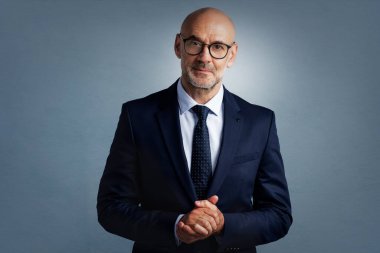 Mavi arka planda dikilirken takım elbise giyen kendine güvenen işadamının stüdyo portresi. 