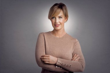 Gri arka planda dikilirken kameraya bakan güzel sarı saçlı kadının stüdyo portresi..