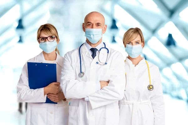 女性と男性の医師の顔のマスクを身に着けていると一緒に病院のホワイエに立ってカメラを見ながら — ストック写真