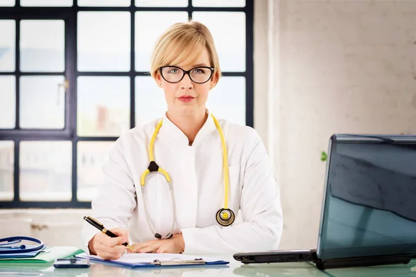 Retrato Sorrir Médico Sentado Mesa Escrever Algo Enquanto Trabalhava Escritório — Fotografia de Stock