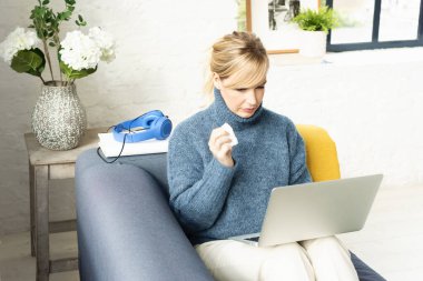 Evdeki kanepede oturup dizüstü bilgisayarında film seyreden üzgün bir kadın..