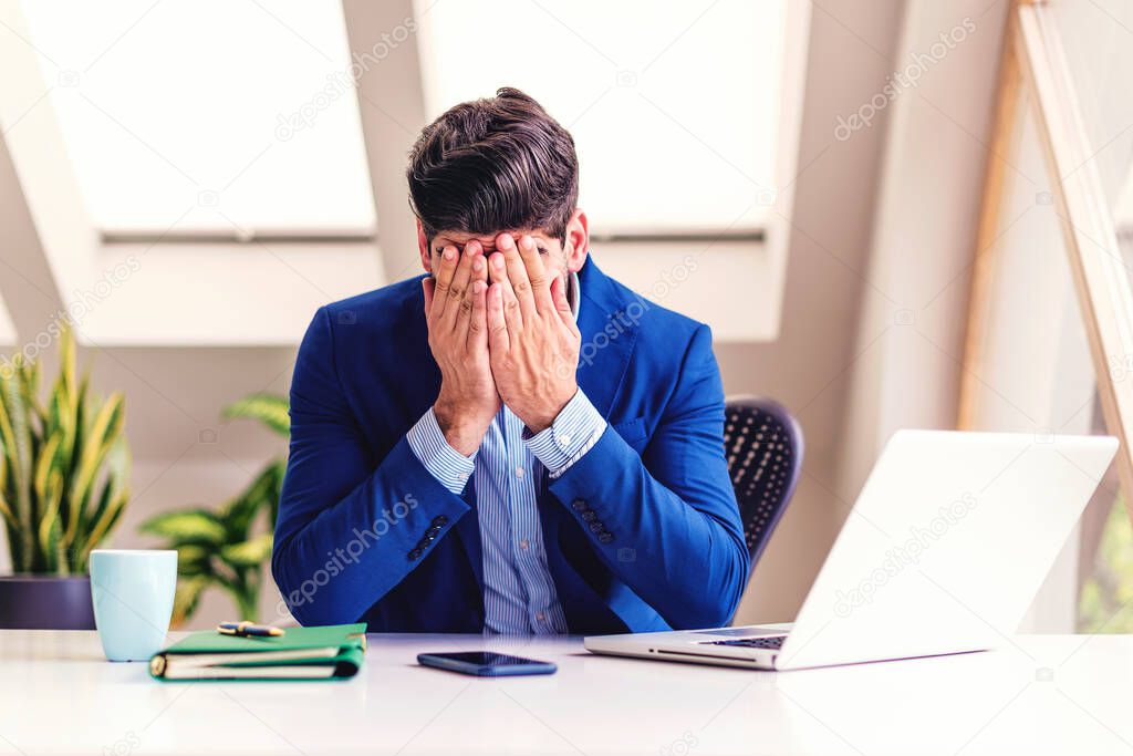 Shot of exhausted businessman with covering his face with her hands while sitting in the office.