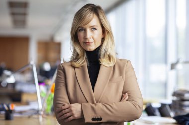 Ofiste kollarını kavuşturmuş dururken balıkçı yaka kazak ve ceket giyen güzel sarı saçlı iş kadını.. 