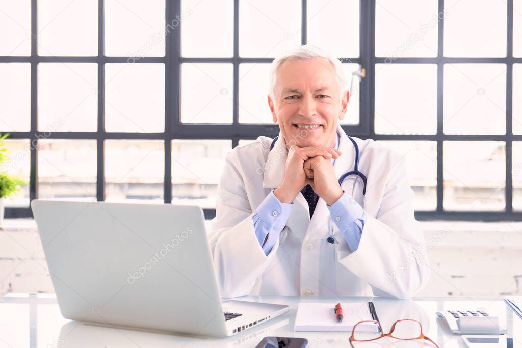 Portrait shot of smiling male doctor working on his laptop in doctor's office. 