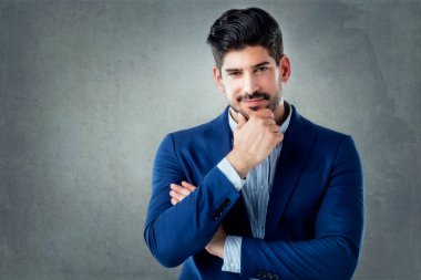Gri arka planda dikilirken düşünceli bir şekilde duran yakışıklı iş adamının stüdyo portresi.. 