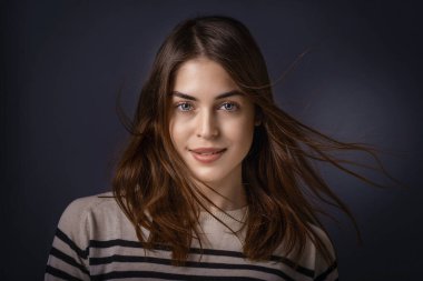 Güzel bir genç kadının stüdyo portresi. Kameraya bakıyor ve izole edilmiş karanlık arka planda dururken gülümsüyor.. 