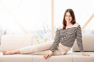 Evdeki kanepede dinlenirken günlük giysiler giyen güzel bir genç kadın..