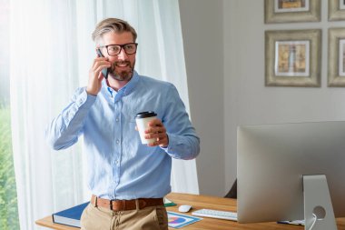 Yakışıklı iş adamının evde çalışırken masasında oturup cep telefonuyla konuştuğu fotoğraf.. 
