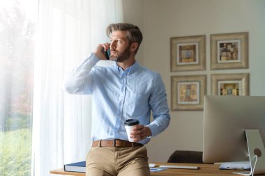 Yakışıklı iş adamının evde çalışırken masasında oturup cep telefonuyla konuştuğu fotoğraf.. 