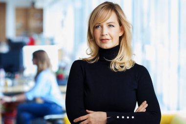 Çekici orta yaşlı iş kadını ofiste kollarını kavuşturmuş duruyor..