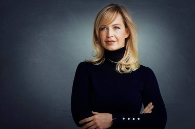 Sarışın, çekici bir kadının portresi. Kolları kapalı, gri arka planda duruyor. Boşluğu kopyala.