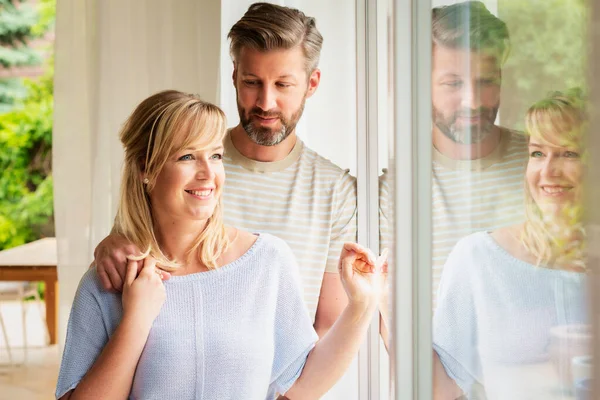 Foto Pareja Feliz Pie Juntos Casa Mientras Mira Por Ventana — Foto de Stock