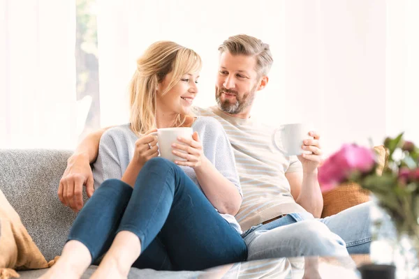 Lovely couple spending qualitiy time together at home while sitting on the sofa and drinking tea.