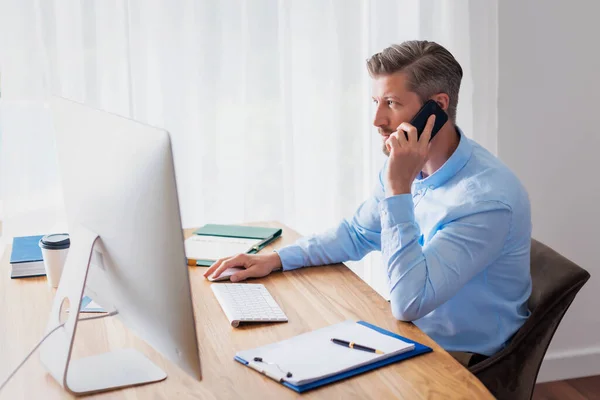 ビジネスマンは自分のコンピュータの後ろに机に座って電話をしている 内務省 — ストック写真
