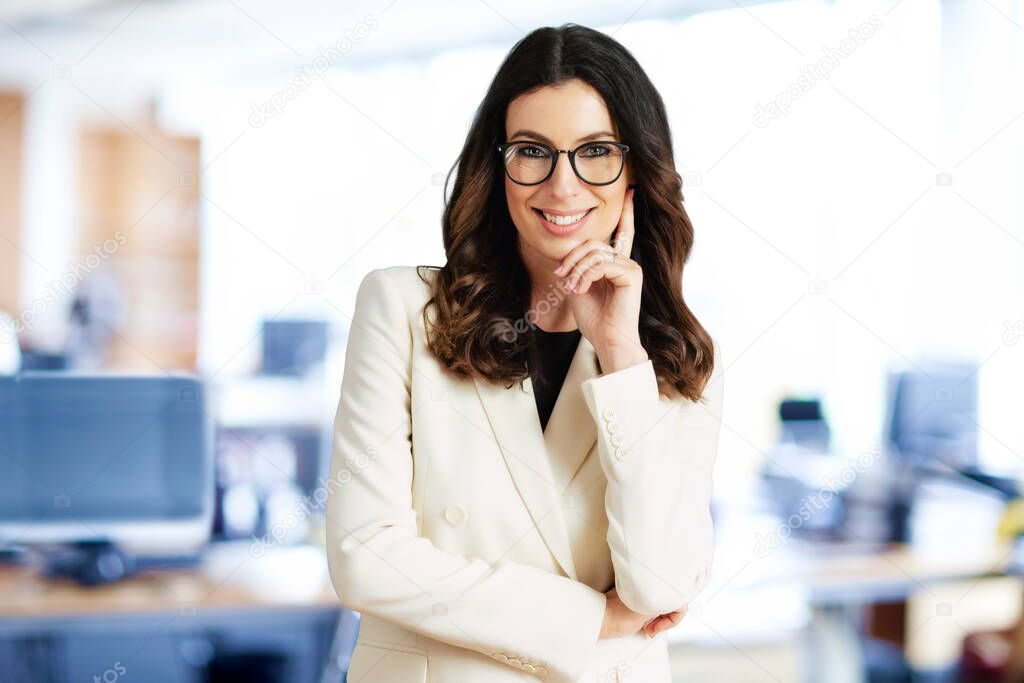 Attractive businesswoman standing at the office while looking at camera and smiling. 