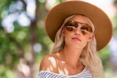 Sokakta otururken güneş gözlüğü ve şapka takan çekici sarı saçlı kızın yakın plan portresi.. 