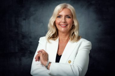 Stüdyo resmi, sarı saçlı yaşlı bir kadının izole edilmiş karanlık arka planda dururken kameraya bakıp gülümsemesi. Boşluğu kopyala.