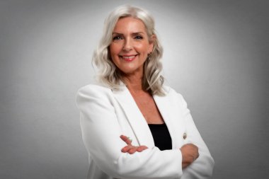 Gri saçlı yaşlı kadının stüdyo portresi. Kameraya bakıyor ve gri arka planda dikilirken gülümsüyor. Boşluğu kopyala.