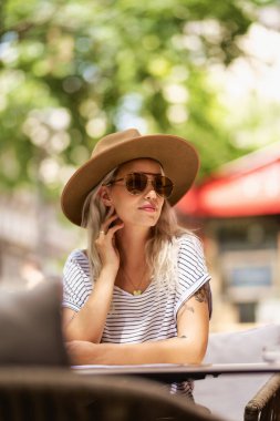 Sokakta otururken güneş gözlüğü takan ve şapka takan çekici sarı saçlı kız.. 