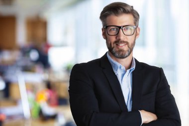 Ofiste kolları çapraz dururken gömlek ve takım elbise giyen orta yaşlı yakışıklı işadamının portresi. Boşluğu kopyala.