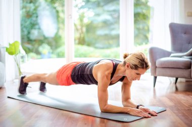Evde vücut egzersizi yapan bir kadının fotoğrafı. Yoga minderinin üzerinde sportif kadın tahtası. Sağlıklı yaşam tarzı.