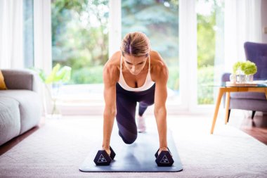 Evde vücut egzersizi yaparken bir kadının dambıl kullanması. Yoga minderinde egzersiz yaparken spor giyen bir kadın. Sağlıklı yaşam tarzı.