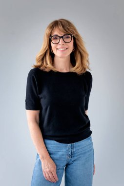 Sarışın kadın, izole edilmiş arka planda duruyor ve kameraya bakıyor. Siyah kazak ve kot pantolon giyen orta yaşlı bir kadın. Boşluğu kopyala. 