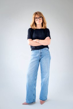 Sarışın kadın, izole edilmiş arka planda duruyor ve kameraya bakıyor. Siyah kazak ve kot pantolon giyen orta yaşlı bir kadın. Uzayı kopyala Tam uzunluk. 