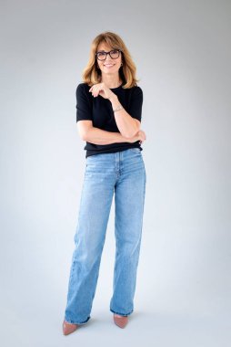 Sarışın kadın, izole edilmiş arka planda duruyor ve kameraya bakıyor. Siyah kazak ve kot pantolon giyen orta yaşlı bir kadın. Uzayı kopyala Tam uzunluk. 