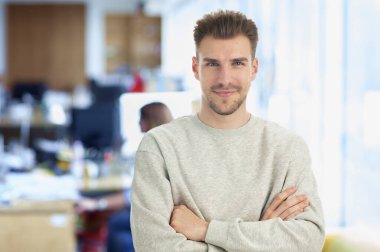 Modern bir ofiste tek başına dururken gülümseyen kendinden emin genç bir iş adamının portresi. Gündelik kıyafetler giyen genç bir girişimci. Yakın çekim.. 
