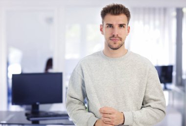 Modern bir ofiste tek başına dururken gülümseyen kendinden emin genç bir iş adamının portresi. Gündelik kıyafetler giyen genç bir girişimci. Yakın çekim.. 