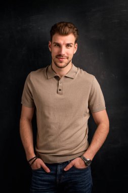 Tecrit edilmiş arka planda duran yakışıklı bir delikanlının yakın çekimi. Uzayı kopyala Polo gömlek ve kot pantolon giyen kendinden emin bir erkek.. 